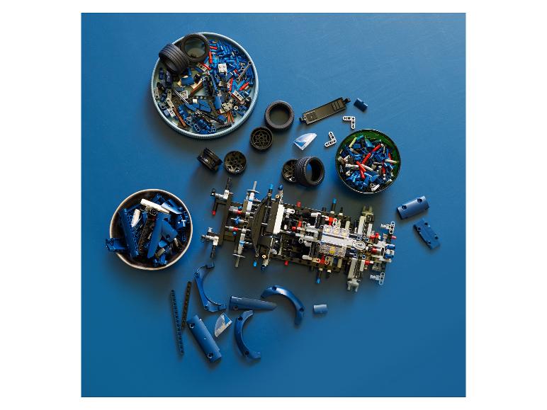 Modré a černé dílky Lego Technic, včetně pneumatik, uspořádané na modrém povrchu.