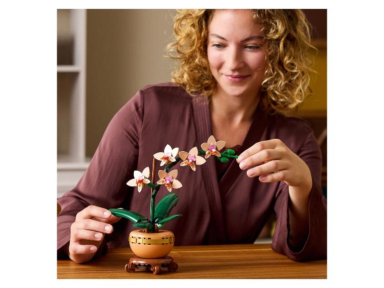 Usmívající se žena se stavební orchidejí na dřevěném stole.