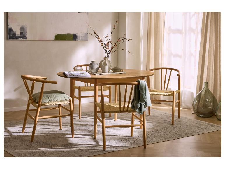 Kulatý dřevěný jídelní stůl se čtyřmi židlemi, kobercem a vázou s květinami.