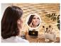 Žena si nanáší make-up před osvětleným zrcadlem, vedle kterého se nabíjí telefon.