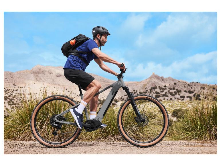 Cyklista na elektrickém horském kole s batohem a helmou v horské krajině.