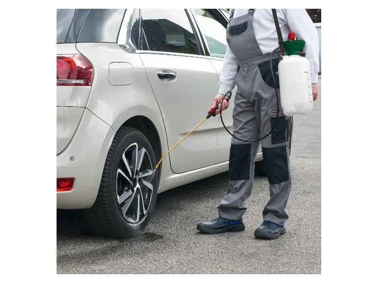 Muž v montérkách čistí pneumatiky auta pomocí tlakového postřikovače.