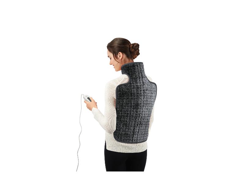 Žena s elektrickou vyhřívací podložkou na záda a krk, držící dálkové ovládání.