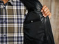 Muž v černé bundě s kostkovanou košilí pod ní.