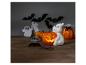 Figurka ducha držící svítící dýni, s halloweenskými dekoracemi.