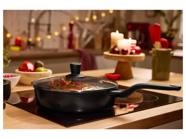 Černá pánev se skleněnou poklicí na varné desce, s vánoční výzdobou v pozadí.