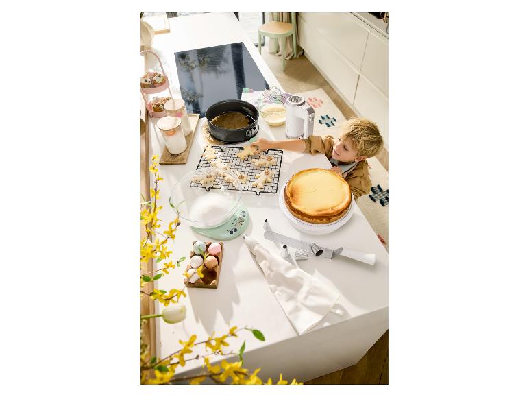 Chlapec zdobí vánoční cukroví na kuchyňské lince s dortem a pekařskými potřebami.