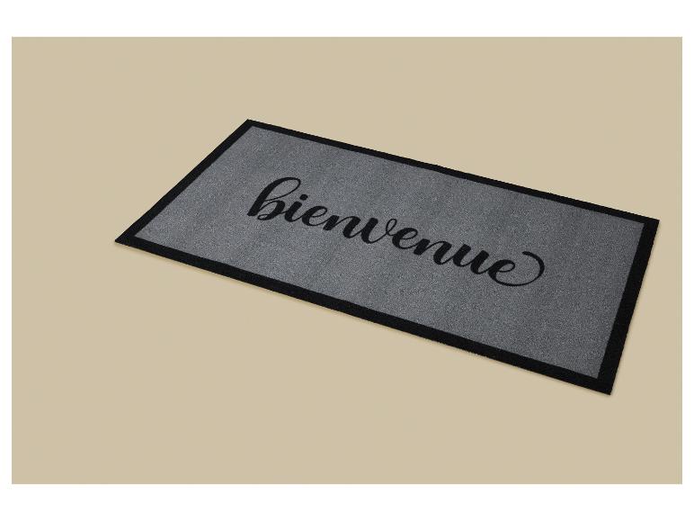 Šedá rohožka s nápisem „bienvenue“ (vítejte) černým kurzívním písmem.
