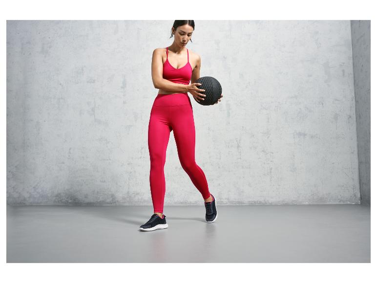 Žena v růžovém sportovním oblečení s černou medicinbalem.