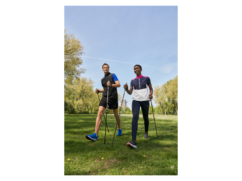 Dva lidé jdou v parku s holemi na nordic walking.