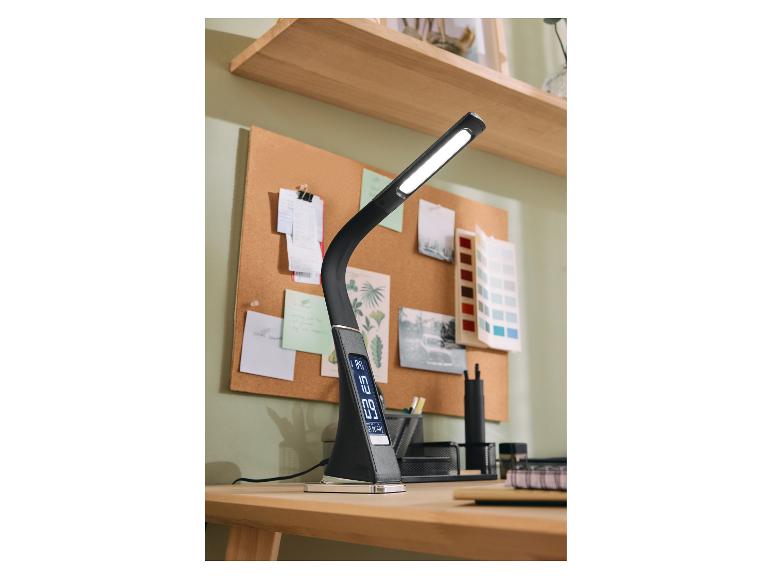 Černá LED stolní lampa s digitálním displejem na dřevěném stole s korkovou nástěnkou.