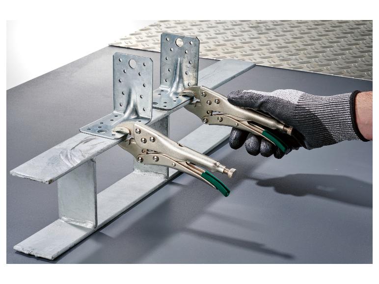 Ruka drží kovovou konzolu kleštěmi, připevněnou k kovovému profilu.