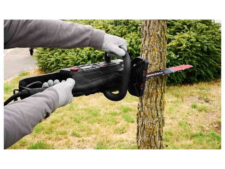 Osoba v rukavicích používá černou elektrickou řetězovou pilu k řezání kmene stromu na zahradě.