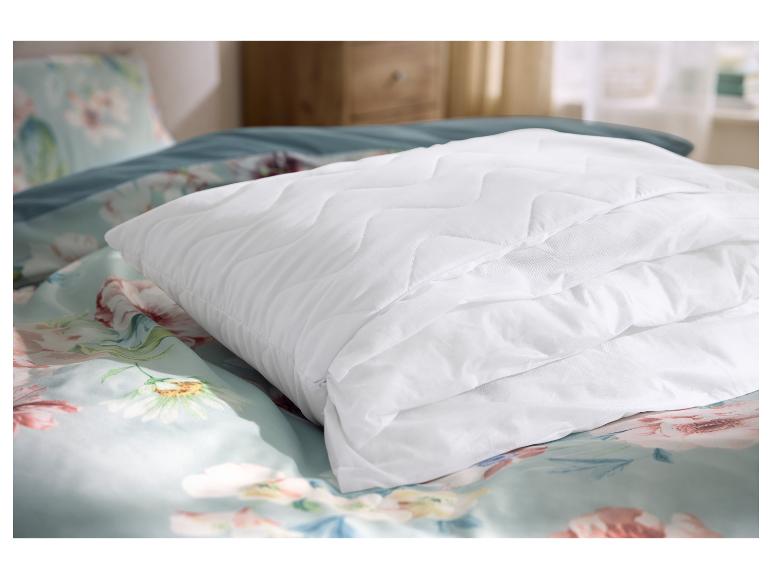 Prošívaný bílý chránič matrace na květinovém povlečení v ložnici.