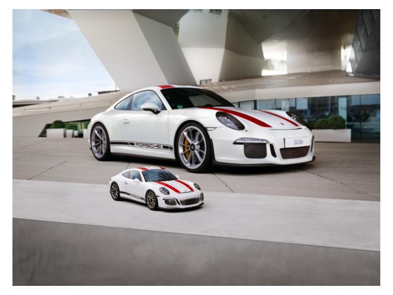 Bílý Porsche 911 GT3 a menší model puzzle před moderní budovou.