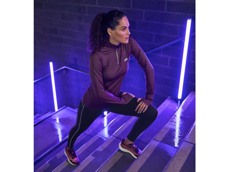 Žena v Reebokovém sportovním oblečení, včetně fialové mikiny a černých legín, cvičí na schodech.