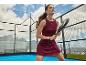 Žena v kaštanových padel šatech s raketou na padel kurtu s horami v pozadí.