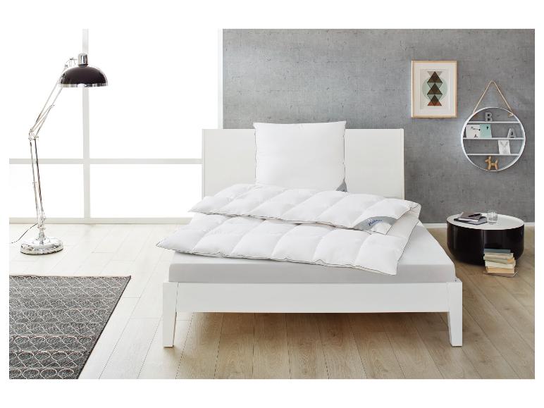 Bílá postel s peřinou a polštářem, čtecí lampa a odkládací stolek v moderní ložnici.