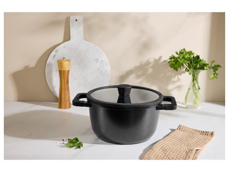 Černý hrnec s poklicí, mlýnek na pepř, krájecí prkénko a petržel v kuchyni.