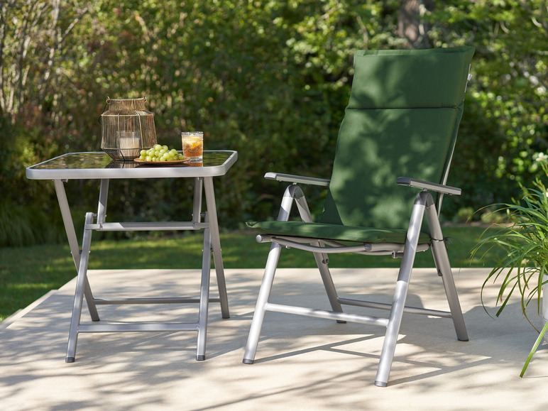 Zelená skládací židle a skleněný stůl s kovovým rámem na terase.