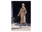 Žena v béžovém trenčkotu a bílých teniskách nese černou crossbody tašku.