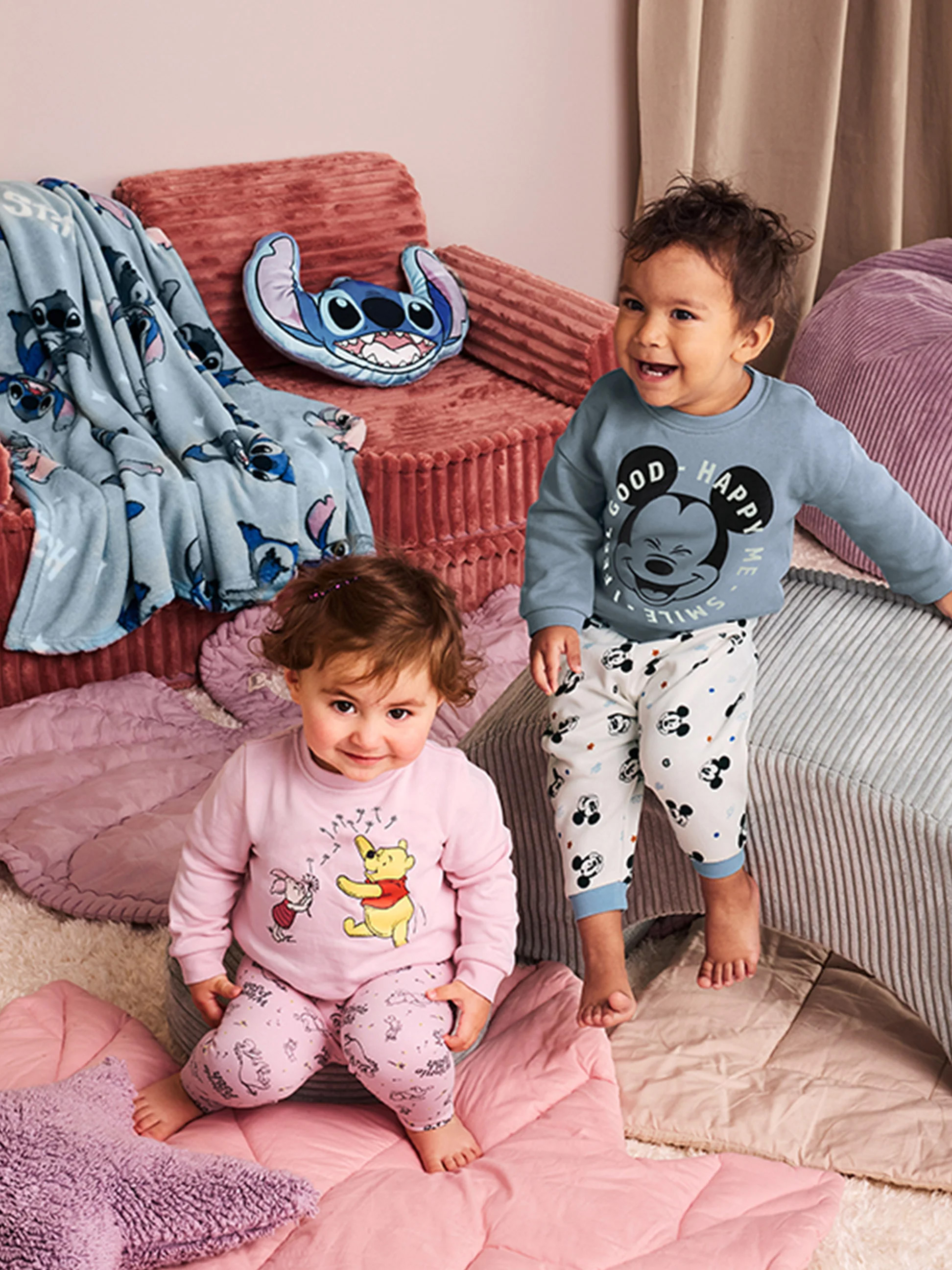 Dvě miminka v pyžamu Disney, obklopená přikrývkami a polštáři Stitch.