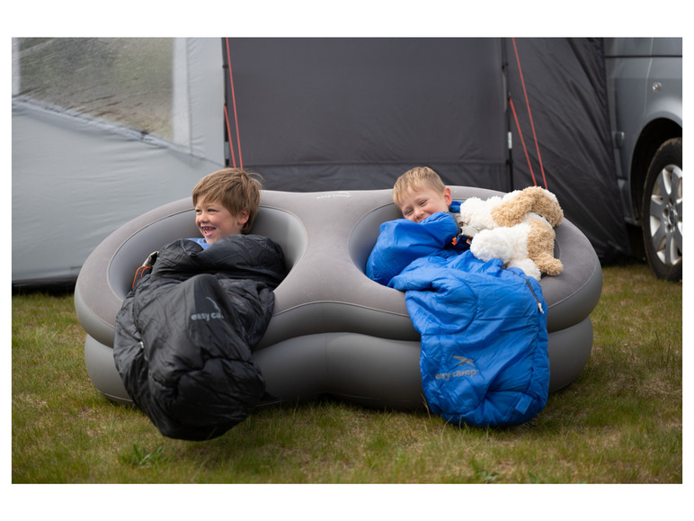Dvě děti ve spacích pytlích Easy Camp v nafukovacím křesle venku.