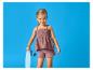 Usmívající se dívka v topu a šortkách barvy slézu, držící světle modrý skateboard.