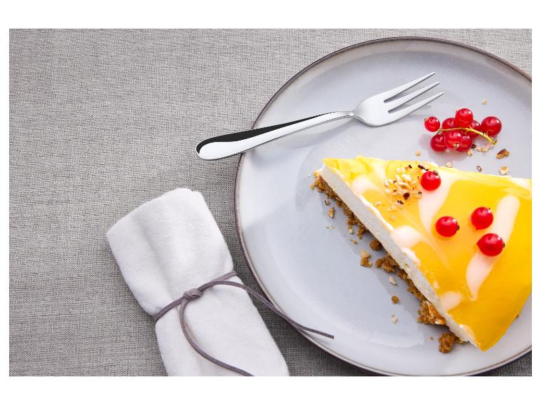 Kousek cheesecaku s mangovou polevou a červeným rybízem na talíři s vidličkou.