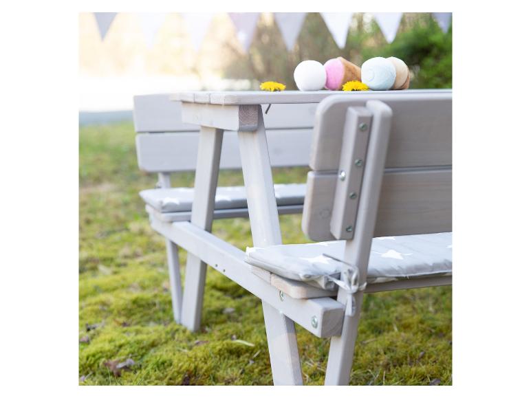 Šedý piknikový stůl s lavicemi a polštáři, zdobený hračkami zmrzliny a pampeliškami.