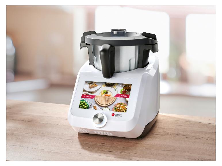 Kuchyňský robot s dotykovým displejem zobrazujícím režimy a recepty, na dřevěném stole.