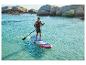 Muž pádluje na paddleboardu v tyrkysové vodě s kamenitým pobřežím v pozadí.