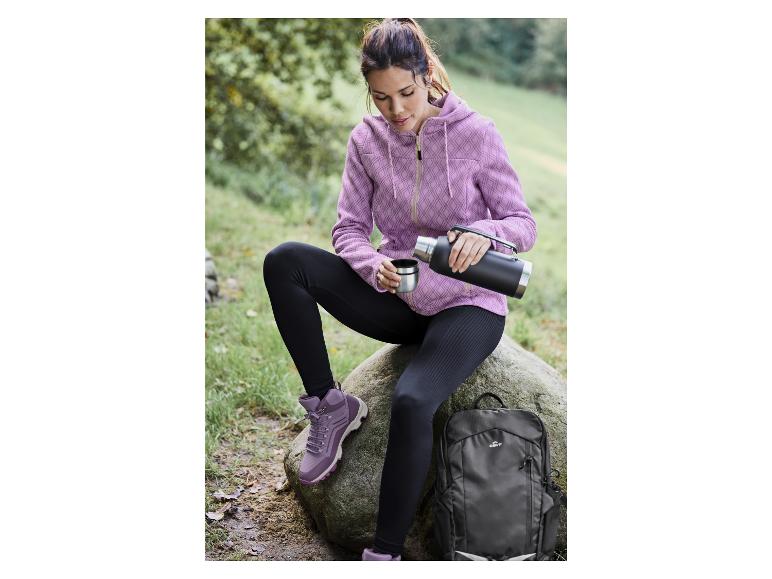 Žena v růžové mikině, černých legínách a turistických botách s termoskou a batohem Crivit.