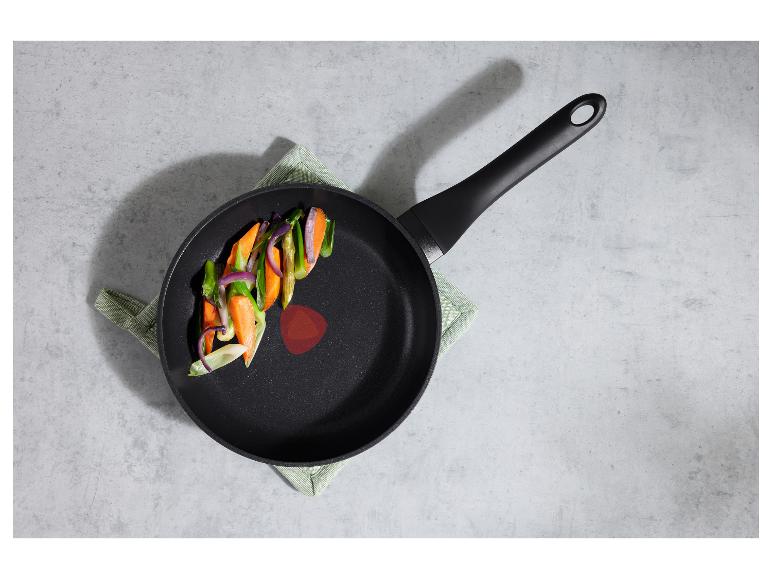 Černá pánev s nakrájenou zeleninou (mrkev, cibule, chřest) na zelené utěrce.