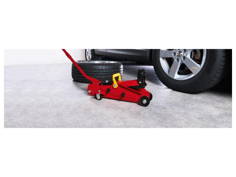 Červený zvedák na auto a pneumatika vedle auta v garáži.