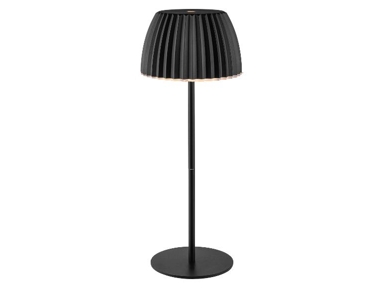 Černá stojací lampa s plisovaným stínidlem, vyzařující teplou záři.