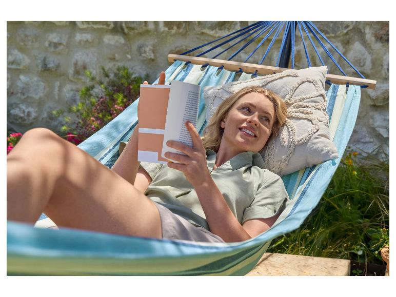 Žena relaxuje v houpací síti s knihou na zahradě.