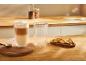 Latte v dvojitostěnném skle a biscotti na dřevěném stole.