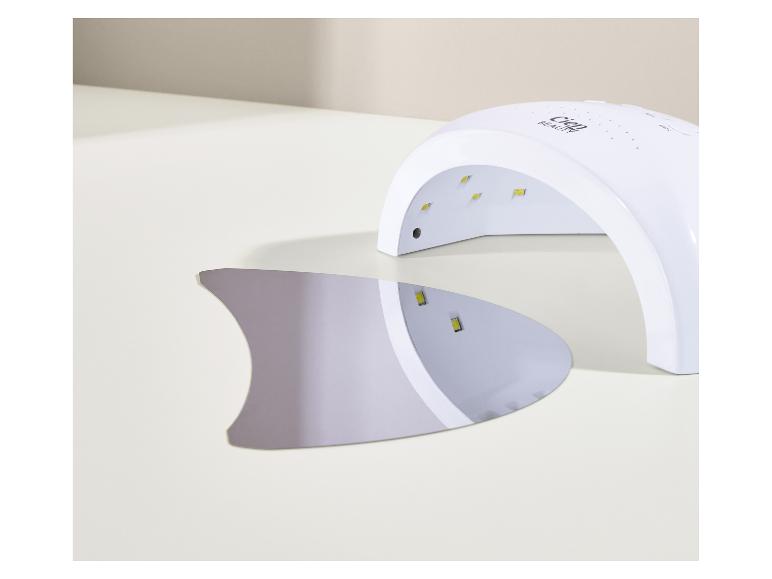 Bílá UV lampa na nehty s odnímatelnou spodní deskou na světlém povrchu.