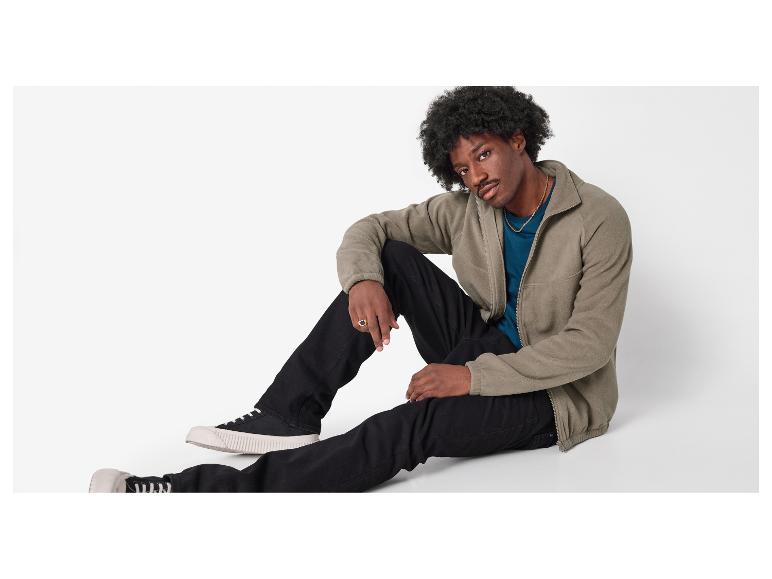 Muž v khaki fleecové bundě, modrém tričku a černých džínách.