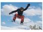 Snowboardista v černé bundě a červených vzorovaných kalhotách ve vzduchu s horami