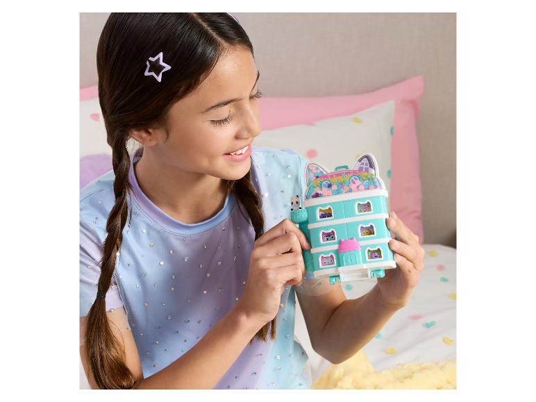 Usmívající se dívka drží kočičí domeček pro panenky s malými figurkami.