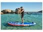 Muž na paddleboardu na čisté vodě, v záchranné vestě, se skalami v pozadí.