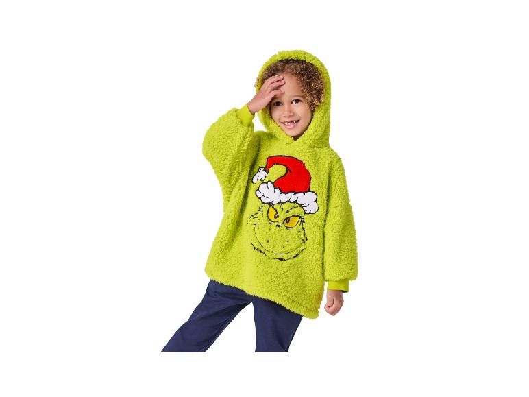 Chlapec v zelené mikině s kapucí Grinch a tmavě modrých kalhotách.
