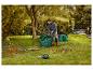 Muž uklízí větve do zelených zahradních pytlů, vedle leží motorová pila.
