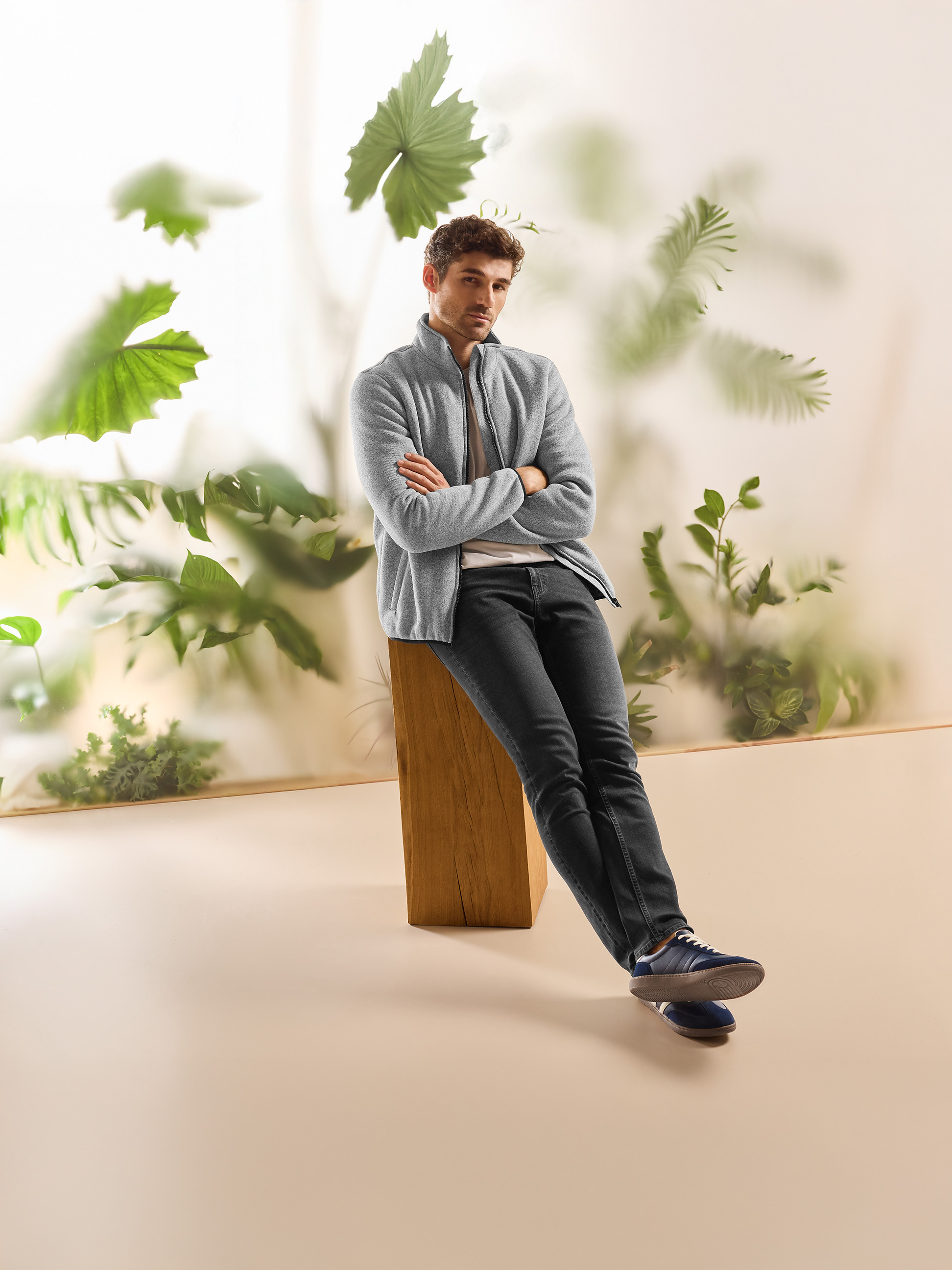 Muž v šedé fleecové bundě a tmavých džínách, sedící v přírodním prostředí.