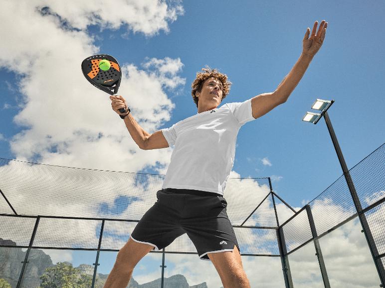 Muž v bílém tričku a černých šortkách hrající padel s raketou a míčkem.
