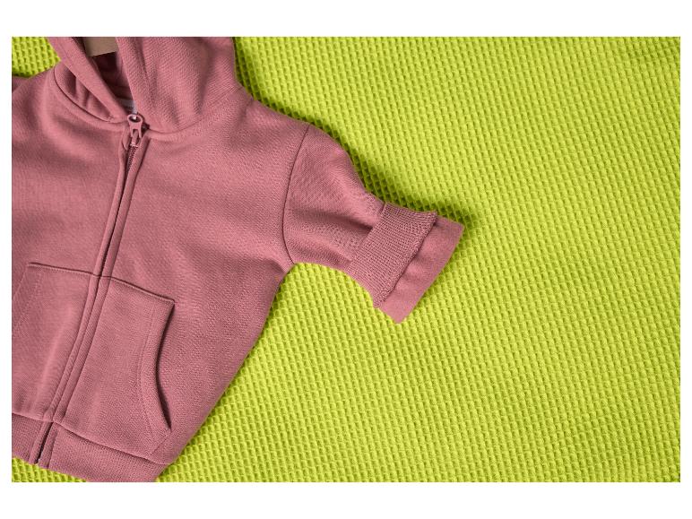 Růžová mikina s kapucí na texturované limetkově zelené dece.