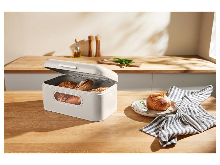 Béžový chlebník s pečivem na dřevěném stole v kuchyni.