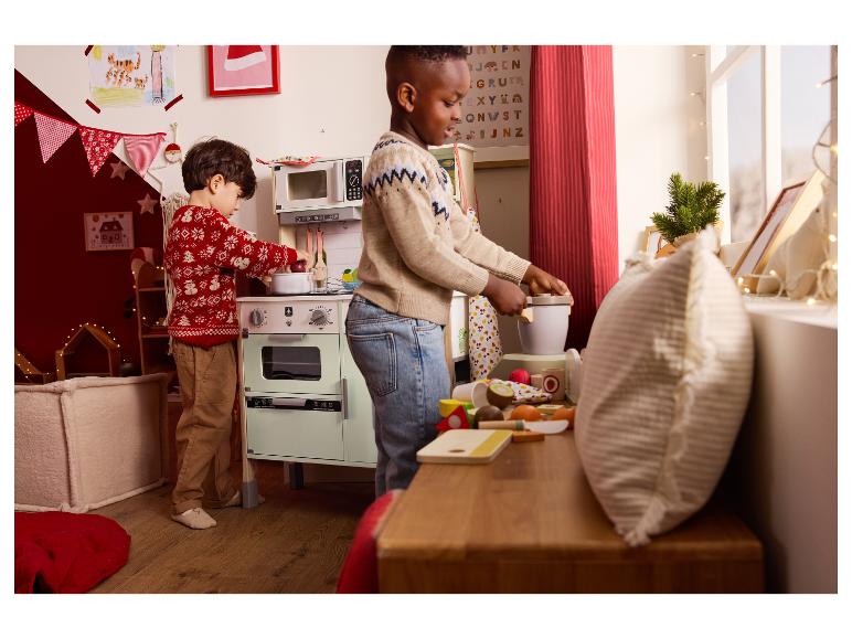 Dvě děti si hrají s hračkářskou kuchyní a dřevěným jídlem.